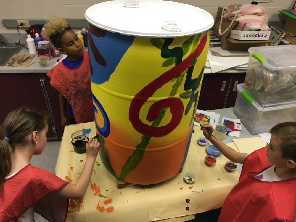three students painting a rain barrel